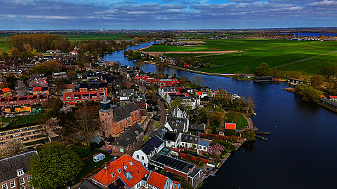 Luchtfoto van een dorp aan het water met weilanden op de achtergrond.