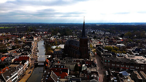 Luchtfoto van een Nederlands dorp met water, brug en woonhuizen.