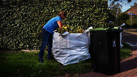 Persoon bezig met tuinzak vullen.