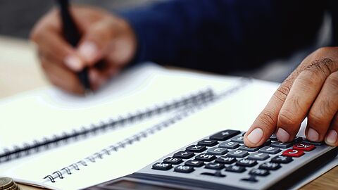 Persoon rekent met rekenmachine en schrijft in notitieboek.