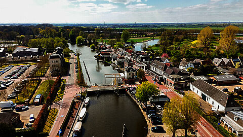 Luchtfoto van een nederlands dorp met water, brug en woonhuizen.