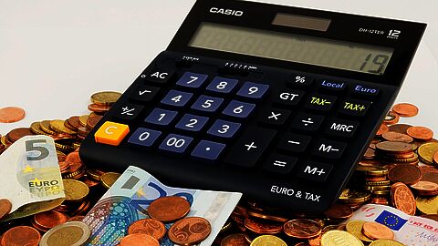 Rekenmachine op een stapel eurobiljetten en euromunten.
